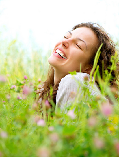 Lepa mlada žena leži u cvetnoj livadi i smeje se