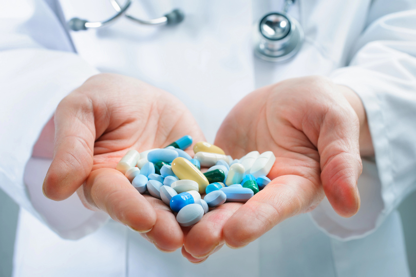 Doktorka drži u rukama pune šake tableta i pilula raznih boja i dimenzija